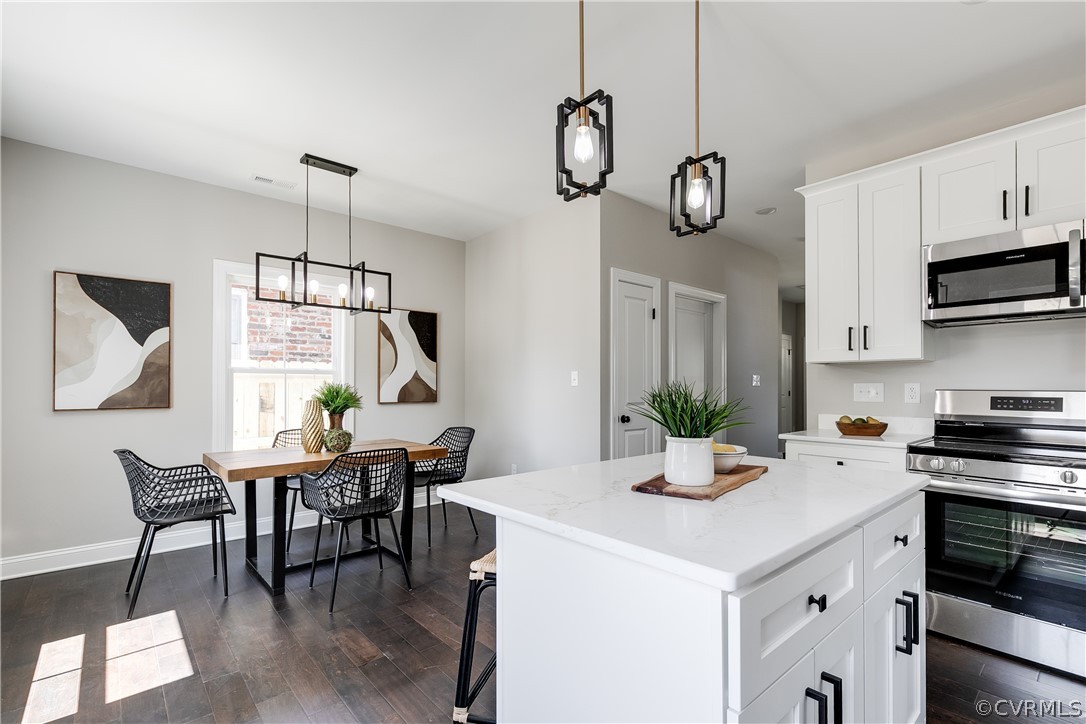 Kitchen with pendant lighting, white cabinets, dark wood-type flooring, appliances with stainless steel finishes, and a kitchen island