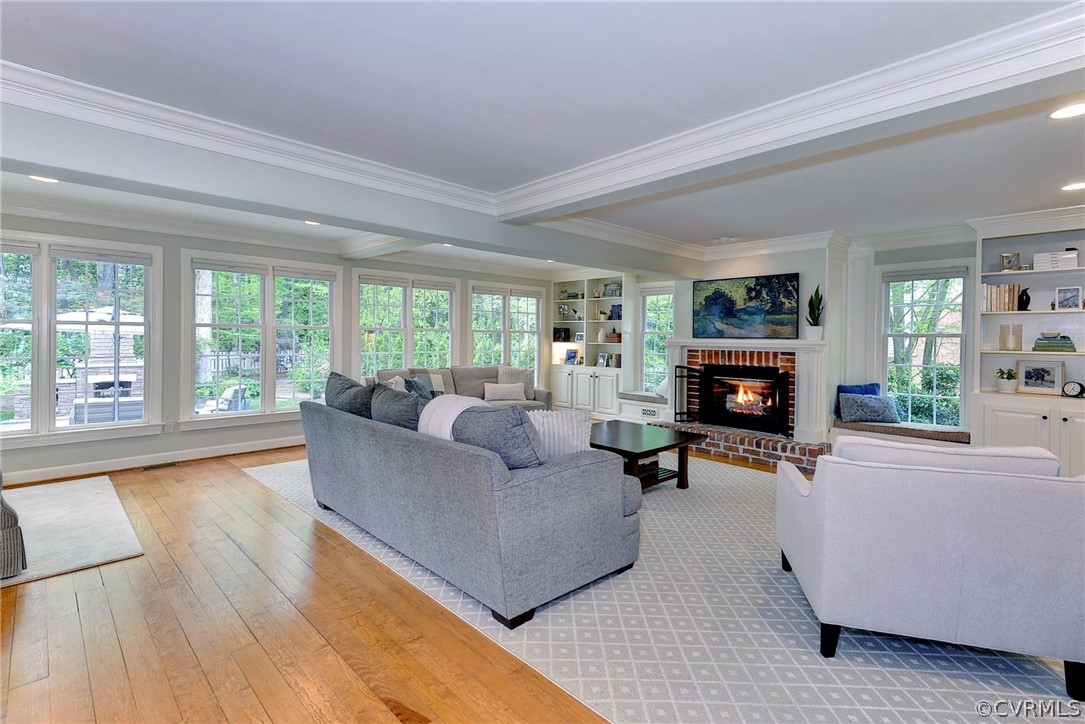Living room featuring a fireplace, crown molding, light wood-type flooring, and plenty of natural light