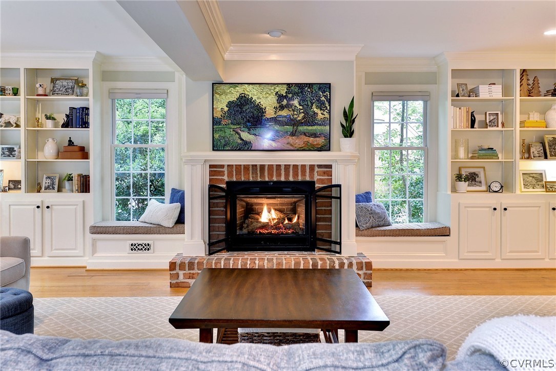 Living room with hardwood / wood-style floors, a brick fireplace, and crown molding