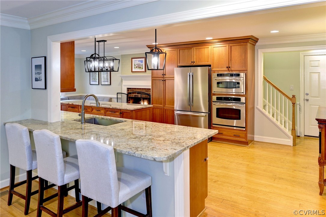 Kitchen with a kitchen bar, sink, light hardwood / wood-style floors, stainless steel appliances, and pendant lighting