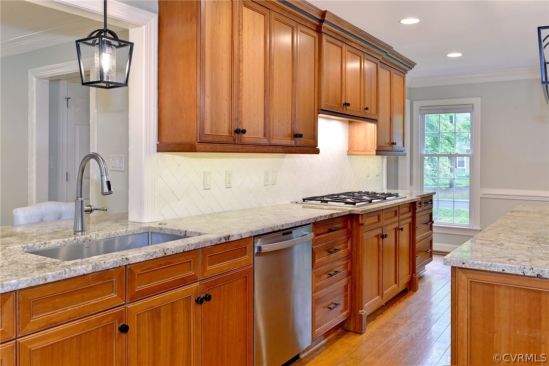 Kitchen featuring appliances with stainless steel finishes, light hardwood / wood-style flooring, hanging light fixtures, backsplash, and ornamental molding