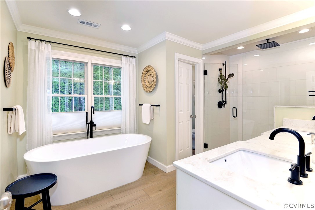 Bathroom with wood-type flooring, independent shower and bath, crown molding, and vanity