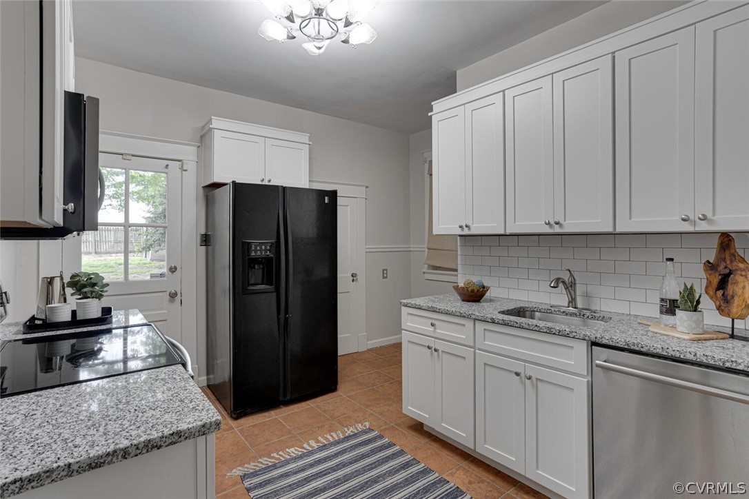 Kitchen with black fridge, backsplash, light tile flooring, dishwasher, and sink