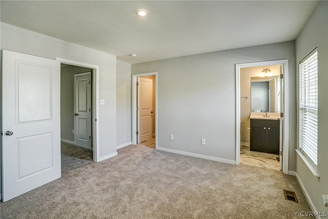 Unfurnished bedroom featuring light colored carpet, connected bathroom, and sink