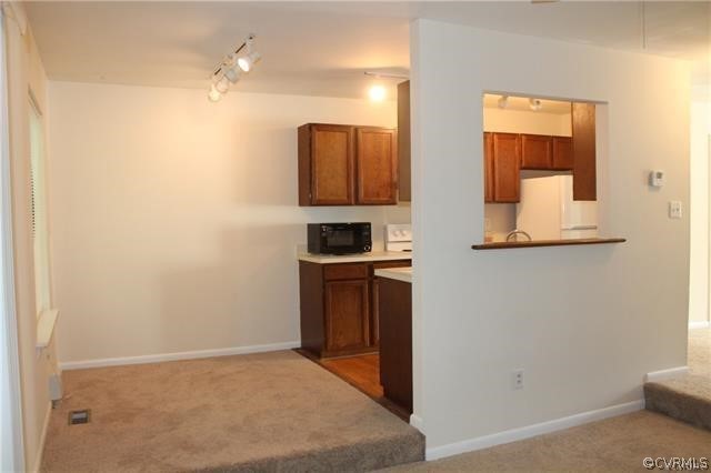 Kitchen featuring rail lighting, white refrigerator, and carpet flooring
