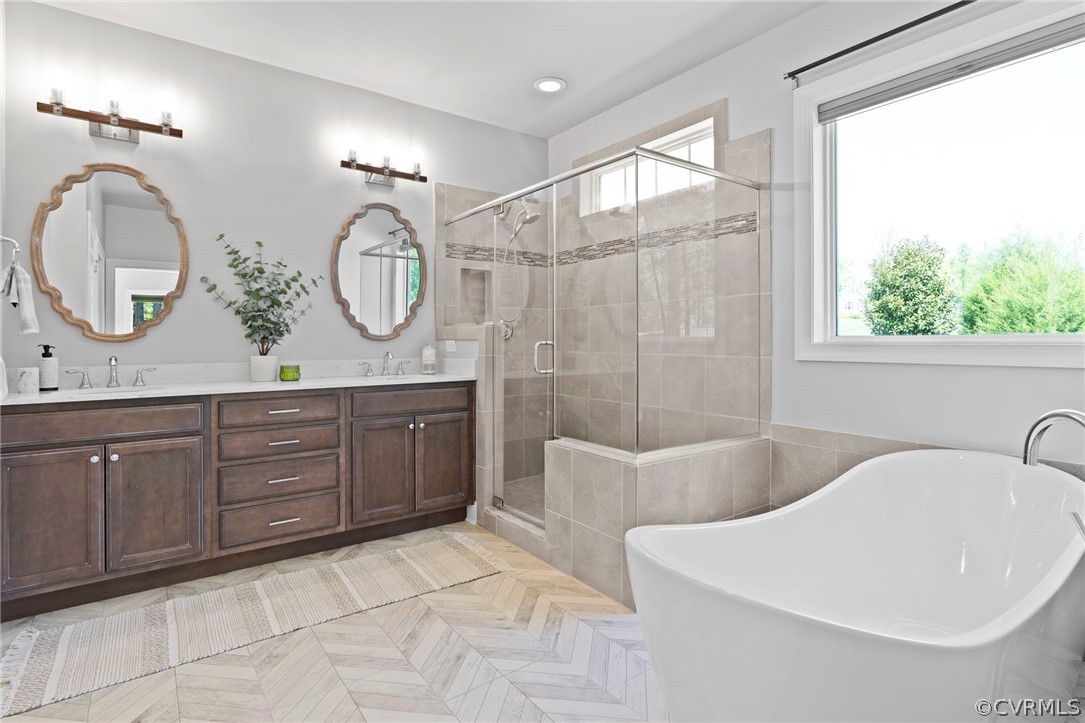Herringbone pattern tile floors, wood frame mirrors, dual vanities, semi-frameless shower, and a large soaking tub by picture window.