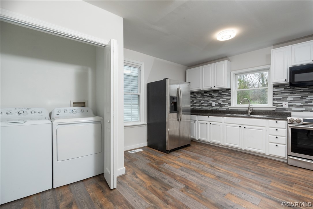 Kitchen featuring washing machine and clothes dryer, backsplash, white cabinetry, dark wood-type flooring, and stainless steel appliances