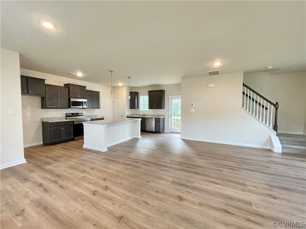 Kitchen with decorative light fixtures, appliances with stainless steel finishes, a center island, and light hardwood / wood-style flooring