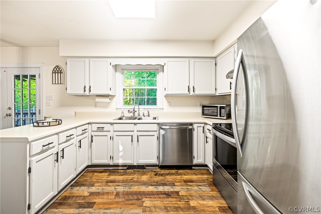 Kitchen with appliances with stainless steel finishes, white cabinets, sink, dark hardwood / wood-style floors, and kitchen peninsula