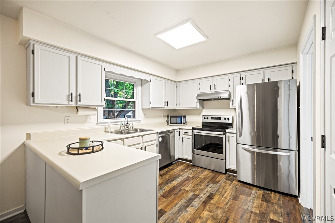 Kitchen with white cabinets, dark wood-type flooring, kitchen peninsula, stainless steel appliances, and sink