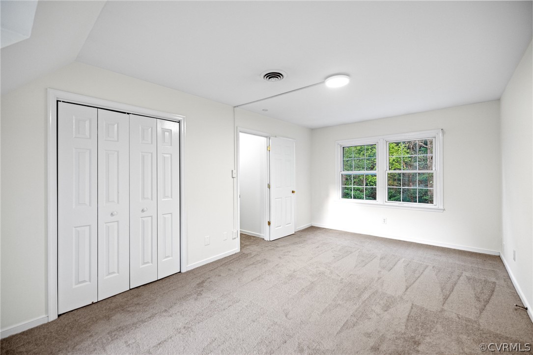 Unfurnished bedroom with light colored carpet, a closet, and vaulted ceiling