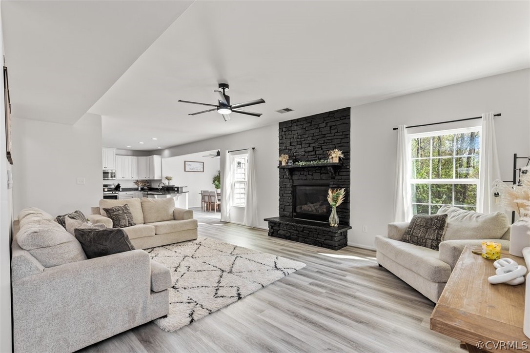 Living room featuring light hardwood / wood-style floors, ceiling fan, and a large fireplace