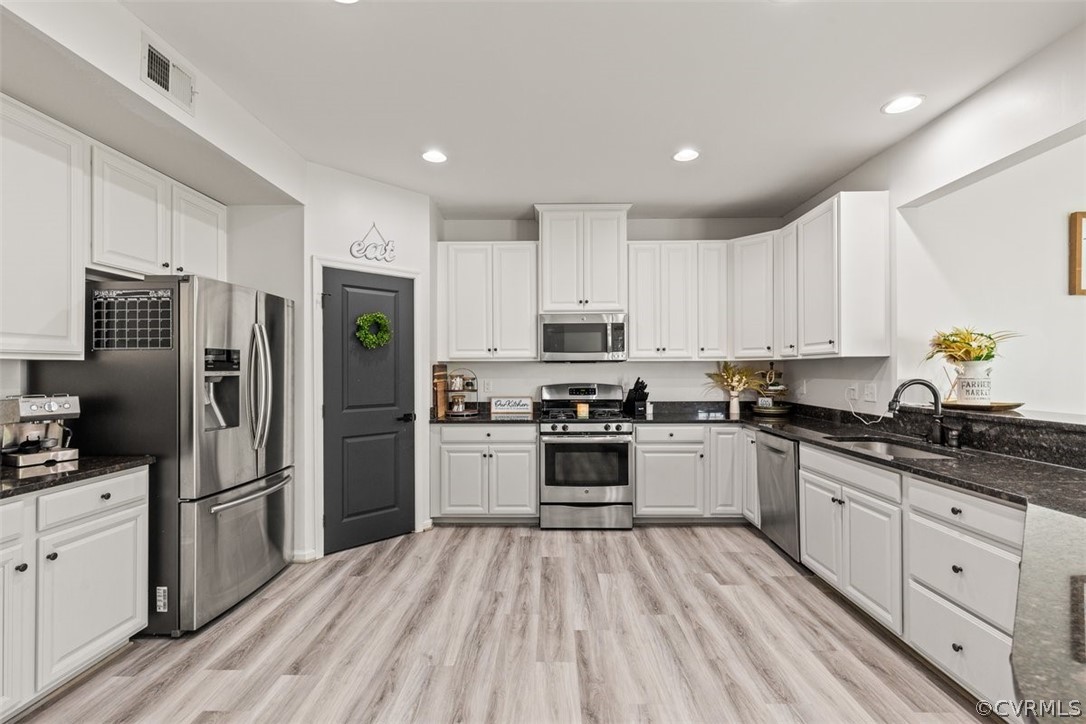 Kitchen featuring white cabinets, sink, dark stone counters, stainless steel appliances, and light hardwood / wood-style flooring