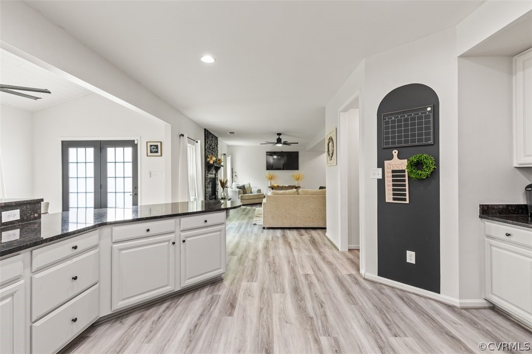 Kitchen with light wood-type flooring, ceiling fan, white cabinetry, and vaulted ceiling