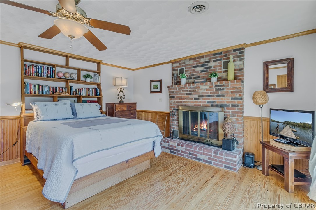 Bedroom with a brick fireplace, light hardwood / wood-style flooring, ceiling fan, brick wall, and ornamental molding