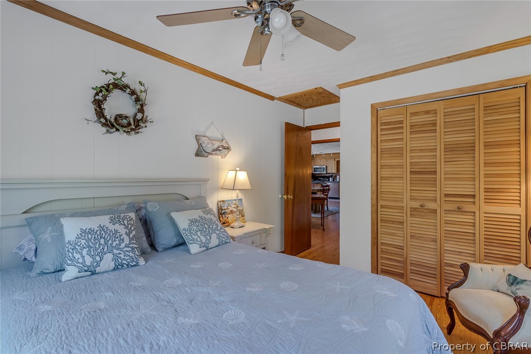 Bedroom featuring hardwood / wood-style floors, a closet, ceiling fan, and crown molding