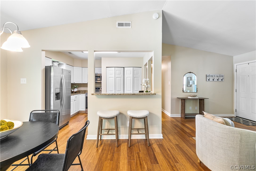 Kitchen featuring vaulted ceiling, appliances with stainless steel finishes, white cabinetry, and hardwood / wood-style flooring