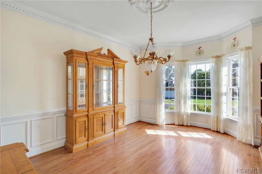 Unfurnished dining area featuring ornamental molding, light hardwood / wood-style floors, and a chandelier