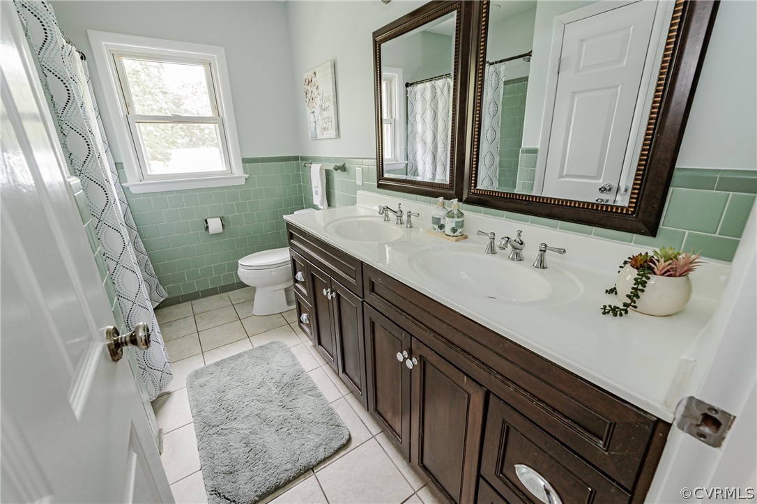 Bathroom featuring toilet, tile flooring, tile walls, and dual vanity