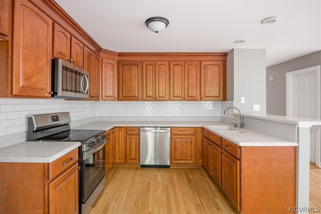Kitchen with appliances with stainless steel finishes, sink, tasteful backsplash, light hardwood / wood-style flooring, and kitchen peninsula