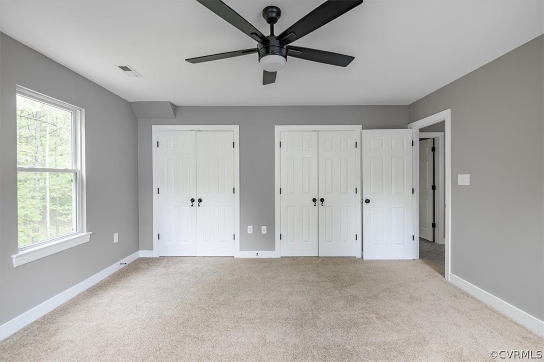 Unfurnished bedroom with light carpet, multiple windows, ceiling fan, and two closets