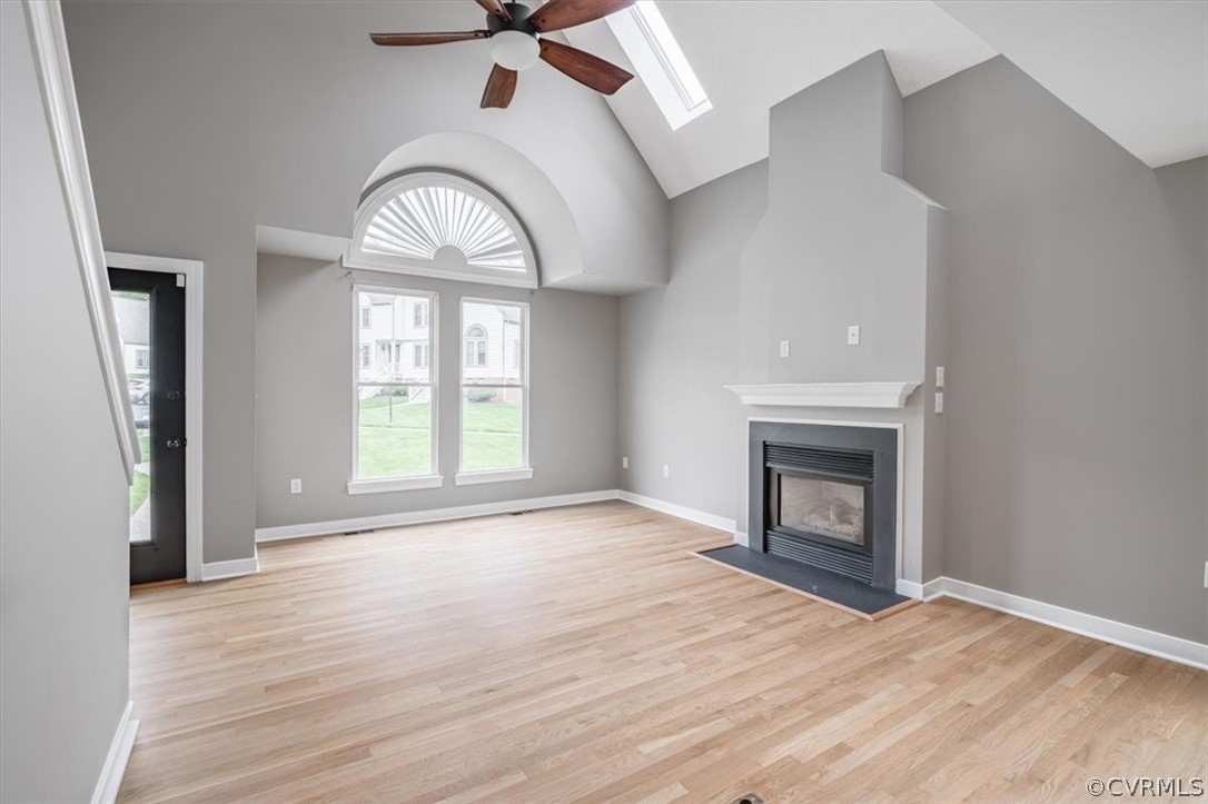 Unfurnished living room featuring a skylight, light hardwood / wood-style flooring, high vaulted ceiling, and ceiling fan