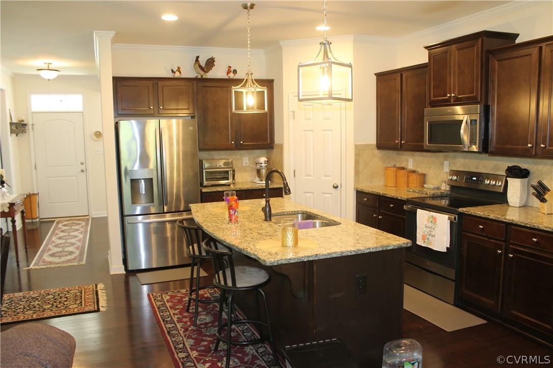 Kitchen featuring backsplash, stainless steel appliances, an island with sink, sink, and dark hardwood / wood-style flooring