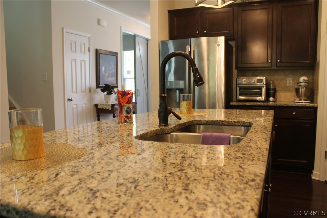 Kitchen featuring light stone counters, sink, backsplash, crown molding, and stainless steel fridge