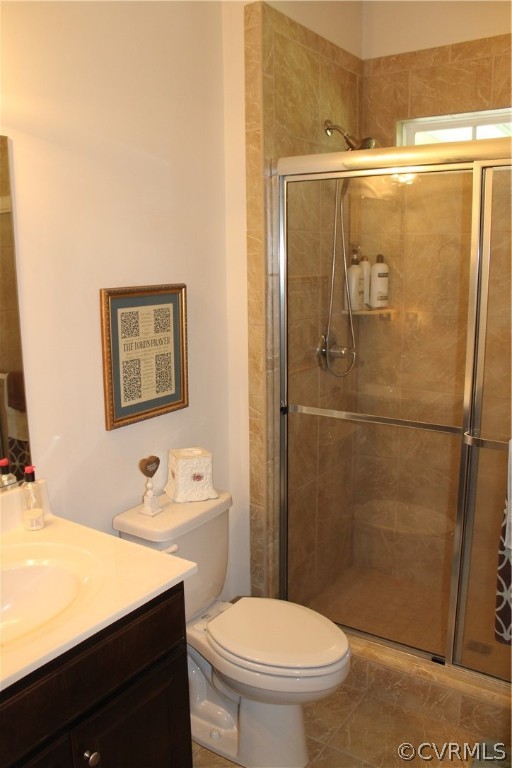 Bathroom featuring a shower with shower door, toilet, tile flooring, and vanity