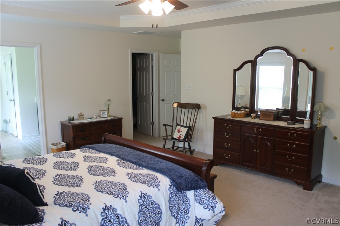 Primary Suite with ceiling fan, a tray ceiling, and ornamental molding