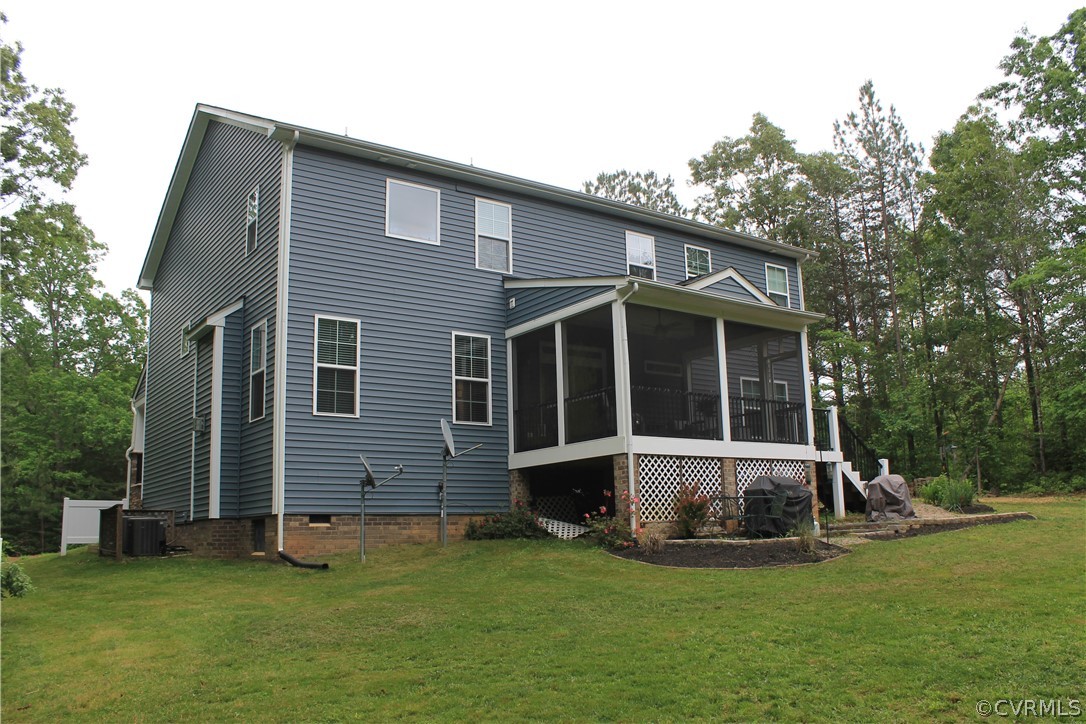 Rear view of property featuring a sunroom, central air condition unit, and a lawn