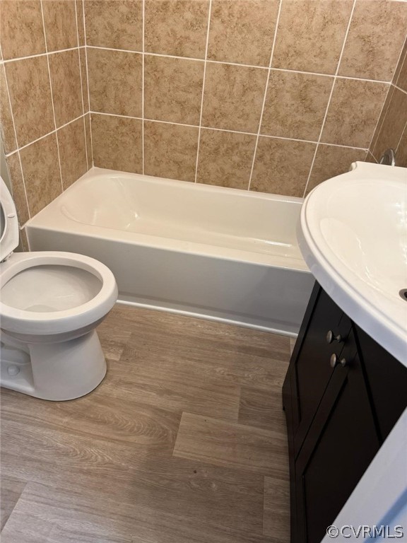 Bathroom with tile walls, hardwood / wood-style floors, vanity, and toilet