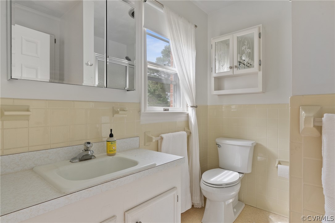 Bathroom with vanity with extensive cabinet space, tasteful backsplash, toilet, and tile walls