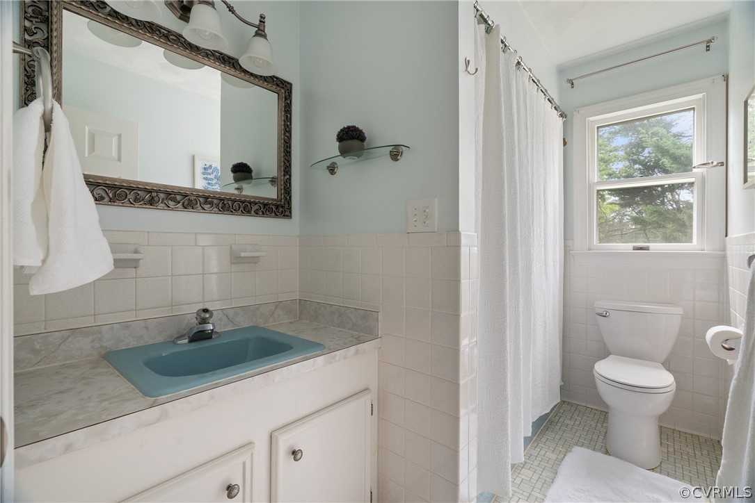 Bathroom featuring tile flooring, tile walls, toilet, and vanity with extensive cabinet space