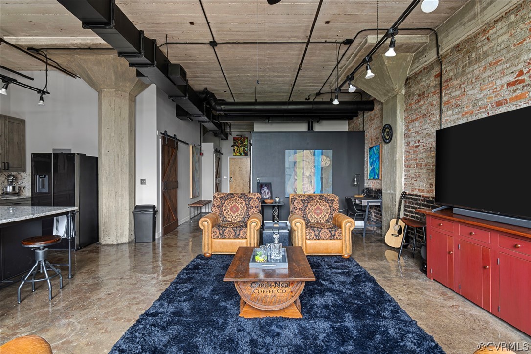 Spacious living room with exposed original brick wall, newly refinished concrete flooring, and  towering industrialized ceiling