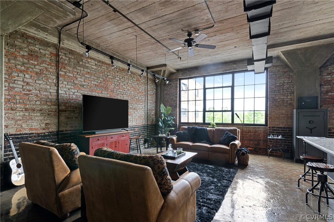 Open concept Living room featuring concrete flooring, ceiling fan, brick wall, and a high ceiling