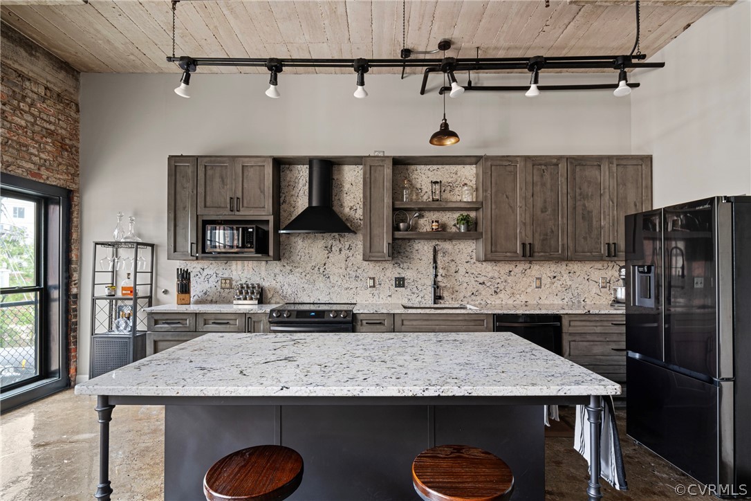 Kitchen featuring wall chimney exhaust hood, a kitchen breakfast bar, decorative light fixtures, and black appliances