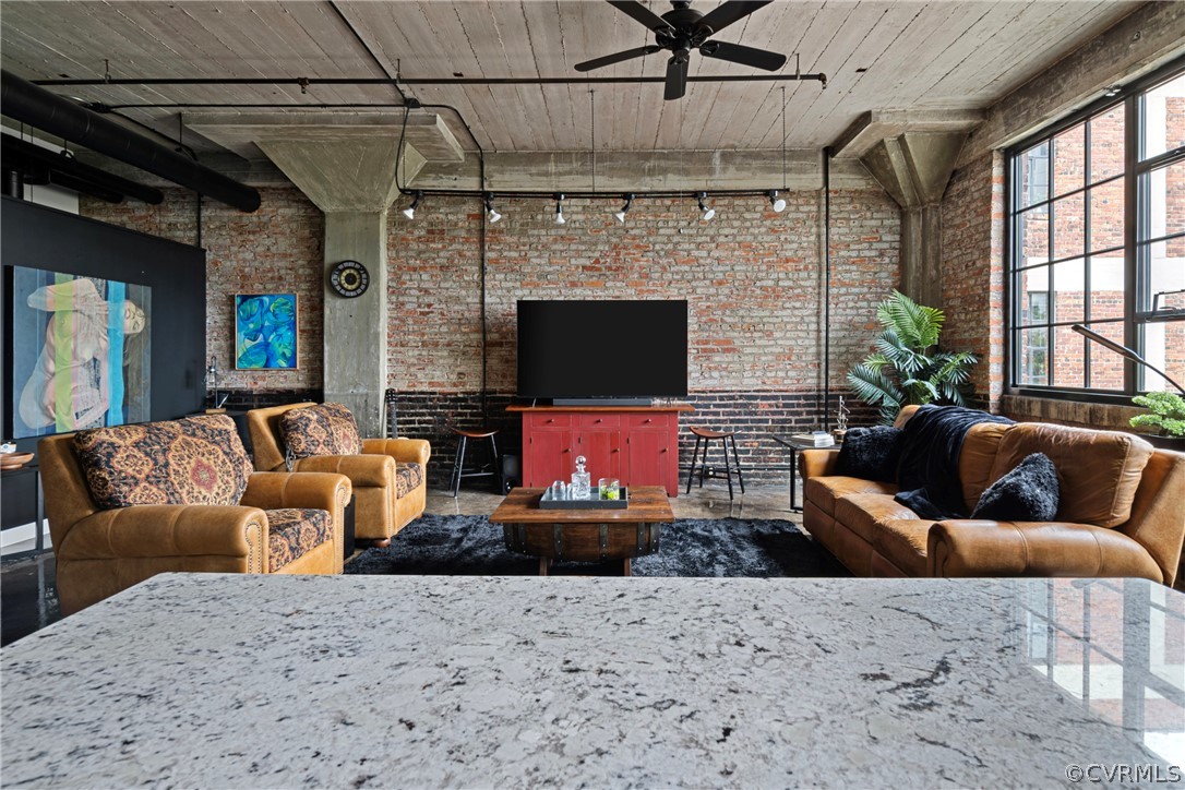 Living room with brick wall, ceiling fan, and track lighting