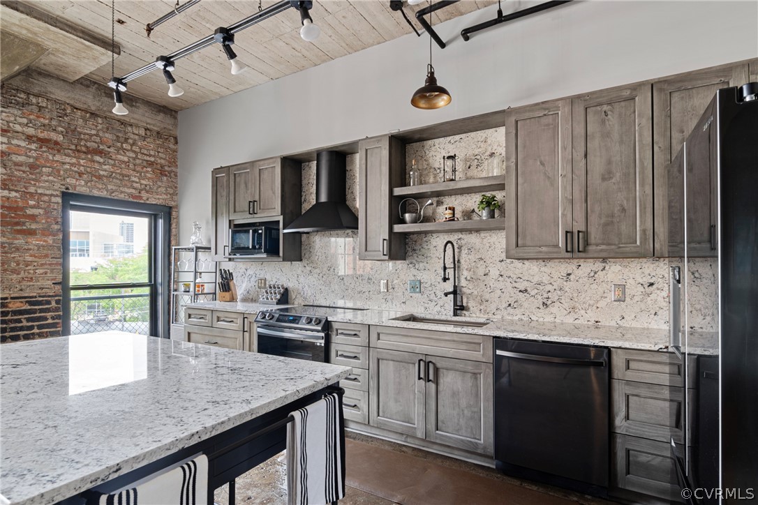Kitchen featuring wall chimney exhaust hood, dishwasher, decorative light fixtures, brick wall, and stainless steel range with electric cooktop