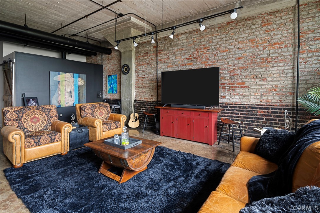 Living room featuring brick wall, rail lighting, and a high ceiling