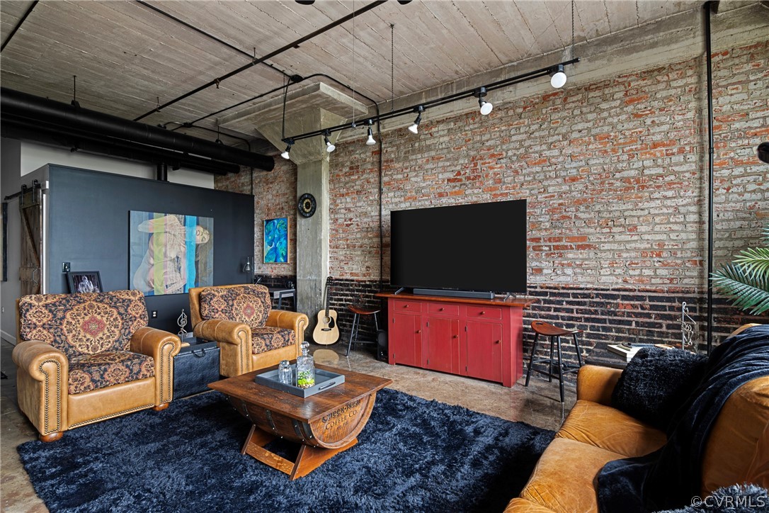 Living room featuring brick wall, a towering ceiling, rail lighting, and concrete flooring