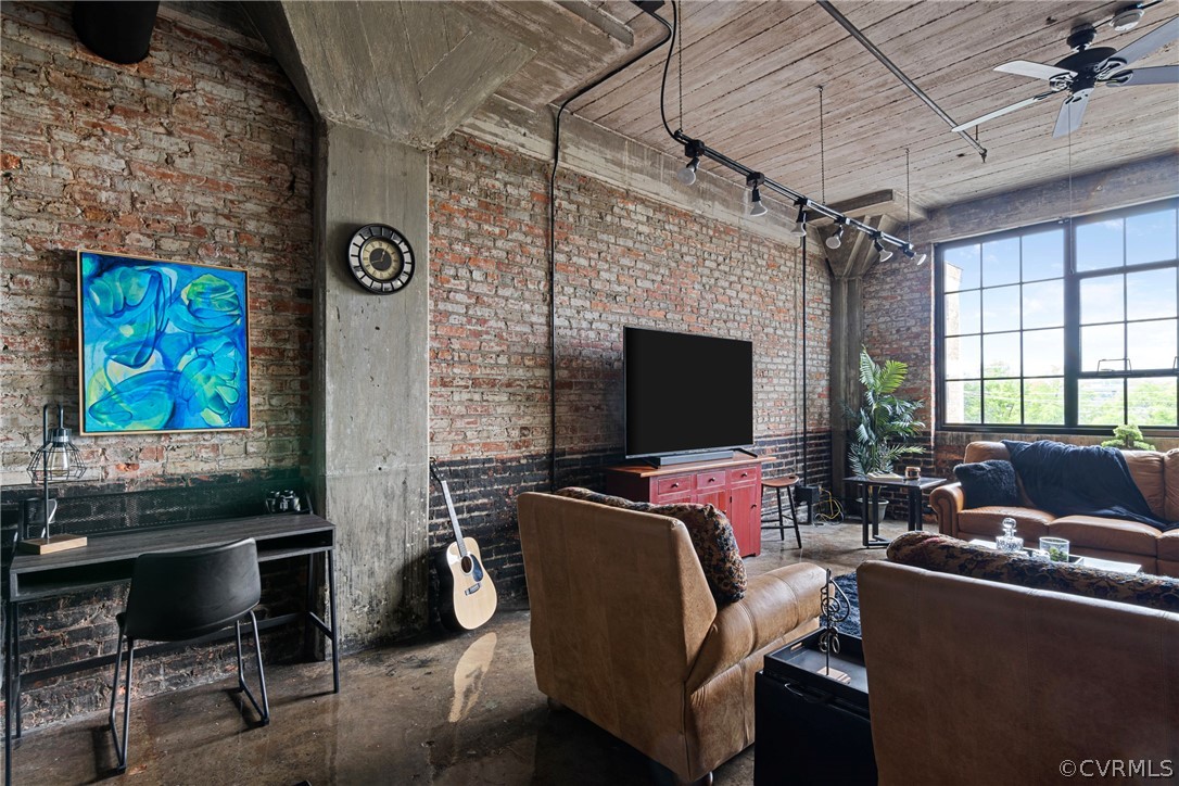 Living room with brick wall, concrete floors, and ceiling fan