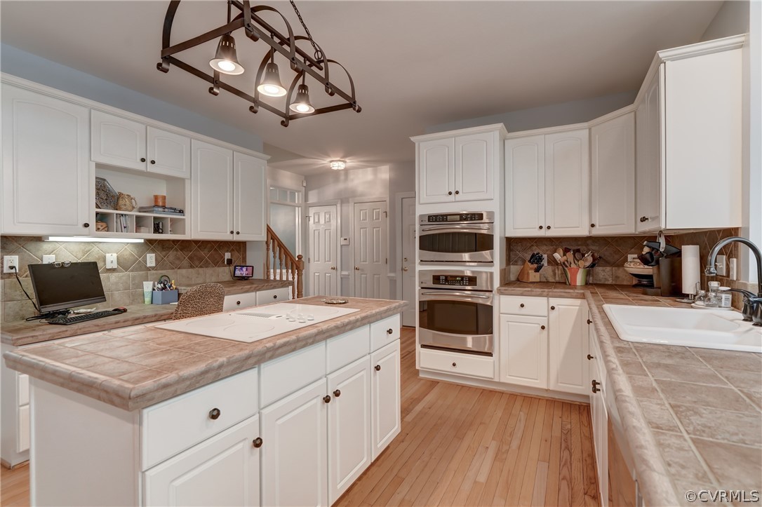 Kitchen with white cabinetry, double oven, tile counters, and backsplash