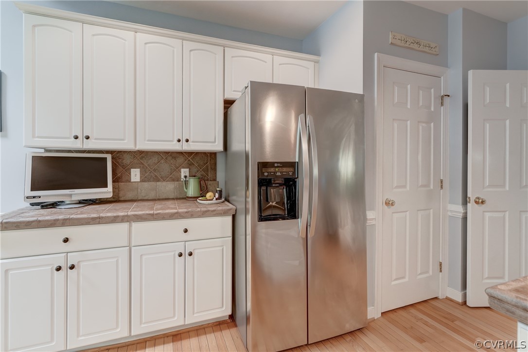 Kitchen featuring stainless steel fridge with ice dispenser, tasteful backsplash, light wood flooring, and white cabinetry
