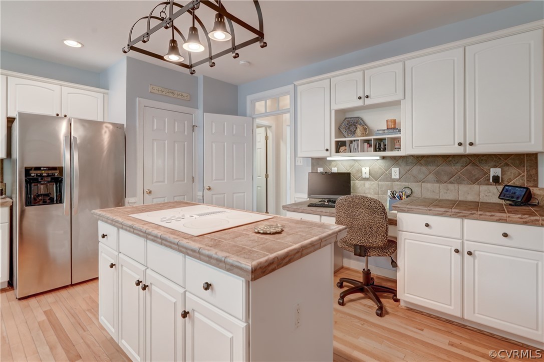 Kitchen with stainless steel fridge with ice dispenser, light hardwood  floors, backsplash, and white cabinetry