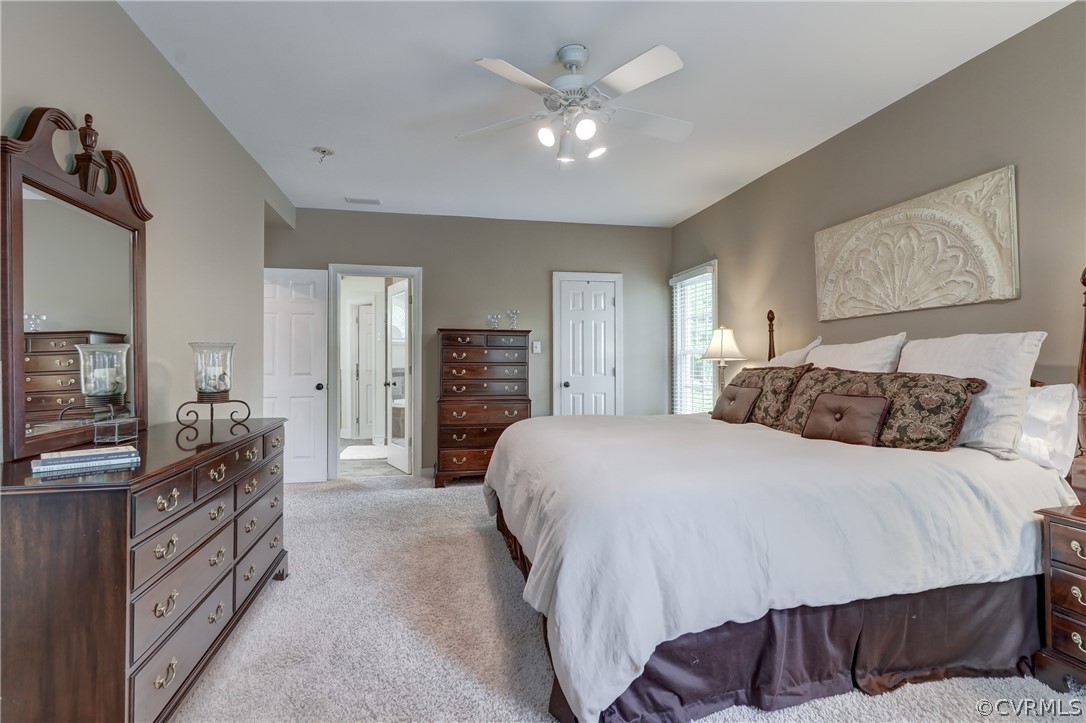 Primary bedroom with light colored carpet, ceiling fan, and a walk in closet