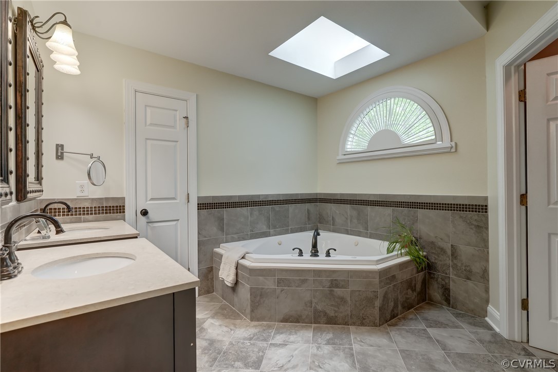 Primary Bathroom with a skylight, tile flooring, dual vanity, and tiled tub
