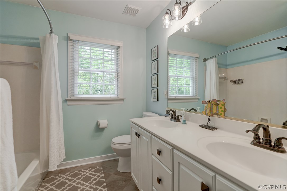 Full bathroom with double vanity, shower / tub combo, a healthy amount of sunlight, and toilet