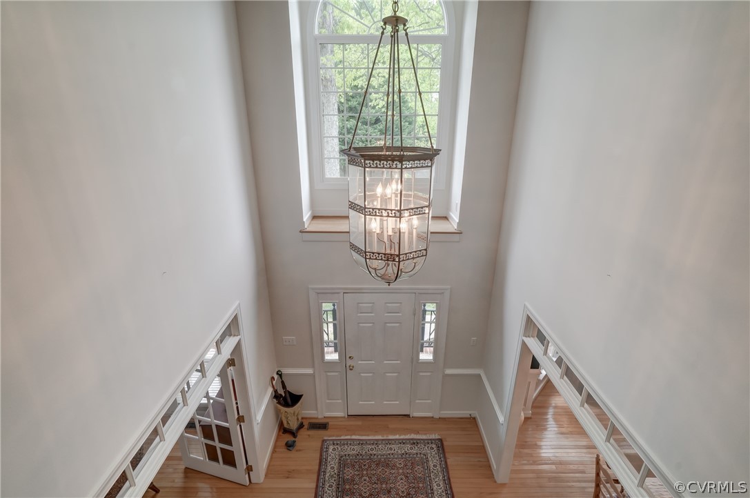Foyer viewed from Balcony featuring wood flooring, a towering ceiling, a wealth of natural light, and an inviting chandelier