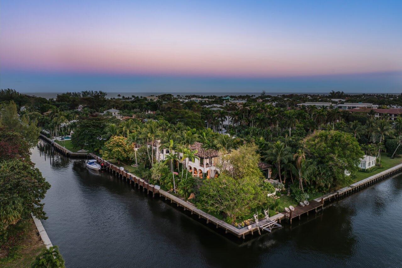 With an extraordinary point-lot position featuring 446'+/- of waterfront, 8 Driftwood Landing stands as one of Gulf Stream's most distinguished properties. Spanning 1.12 acres, this estate represents the pinnacle of coastal living, designed by the renowned Randall Stofft and impeccably finished by the acclaimed Marc Michaels Interiors. Every detail reflects a harmonious blend of refinement, sophistication, and comfort. This thoughtfully crafted residence offers 7,293 square feet under air, with a gracious layout designed to maximize panoramic water views and seamless indoor-outdoor living. The estate includes five en-suite bedrooms, two half bathrooms, and a private guest house complete with its own bedroom, bath, living area, and kitchen--perfect for hosting guests in style and privacy. The luxurious second-floor primary suite is a tranquil sanctuary, featuring an expansive balcony overlooking lush gardens and the Intracoastal Waterway. The epicurean kitchen, outfitted with top-tier appliances, flows effortlessly into the sunlit family room and informal dining area, creating an inviting space for casual gatherings. For entertainment, the home features state-of-the-art media and game rooms, while the elegant dining and living rooms provide a refined setting for holiday celebrations and special occasions. The estate is adorned with bespoke finishes, including lavish millwork, soaring ceilings, French doors, and a mix of wood and marble floors. Additional highlights include wet bars, wine storage, a full-house generator, and fireplaces for the occasional cool evening.
Outdoors, this property transforms into a tropical paradise. A five-star resort-style pool, surrounded by lush landscaping and fruit trees, invites relaxation, while the oversized wrap-around loggia with an outdoor kitchen is perfect for alfresco dining and entertaining. For boating enthusiasts, the estate offers two docks, 160' and 40' respectively and a lift, making it a yachtsman's dream. Perfectly situated just moments from pristine beaches, upscale shopping, fine dining, and exciting diversions, this awe-inspiring estate offers unparalleled access to South Florida's finest. With convenient proximity to international airports, your travels will be effortless- but your favorite destination will always be returning home. Don't miss this rare opportunity to own a truly breathtaking property that promises the ultimate coastal lifestyle.